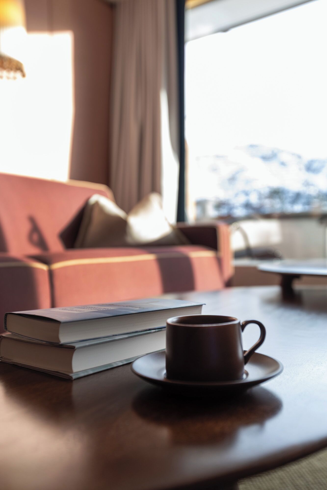 A cozy seating area with a sofa, a table with a cup and a book, and a view of a snowy landscape through a window.