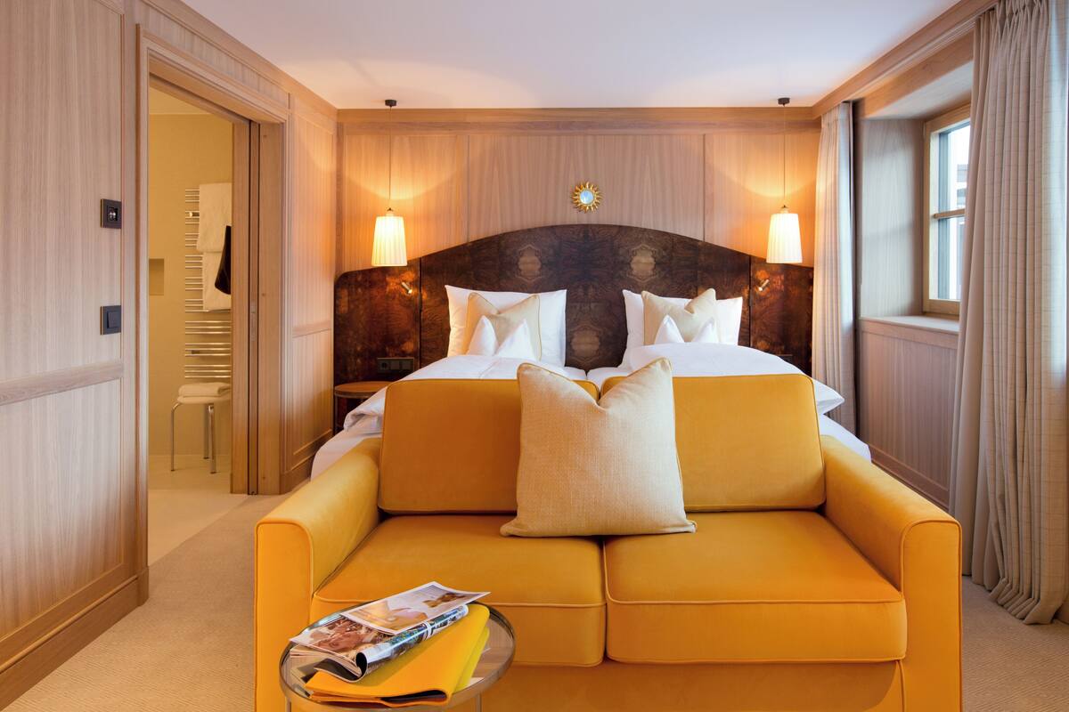 A hotel room with a large bed, a sofa, a small table with a magazine, and two wall-mounted lamps.