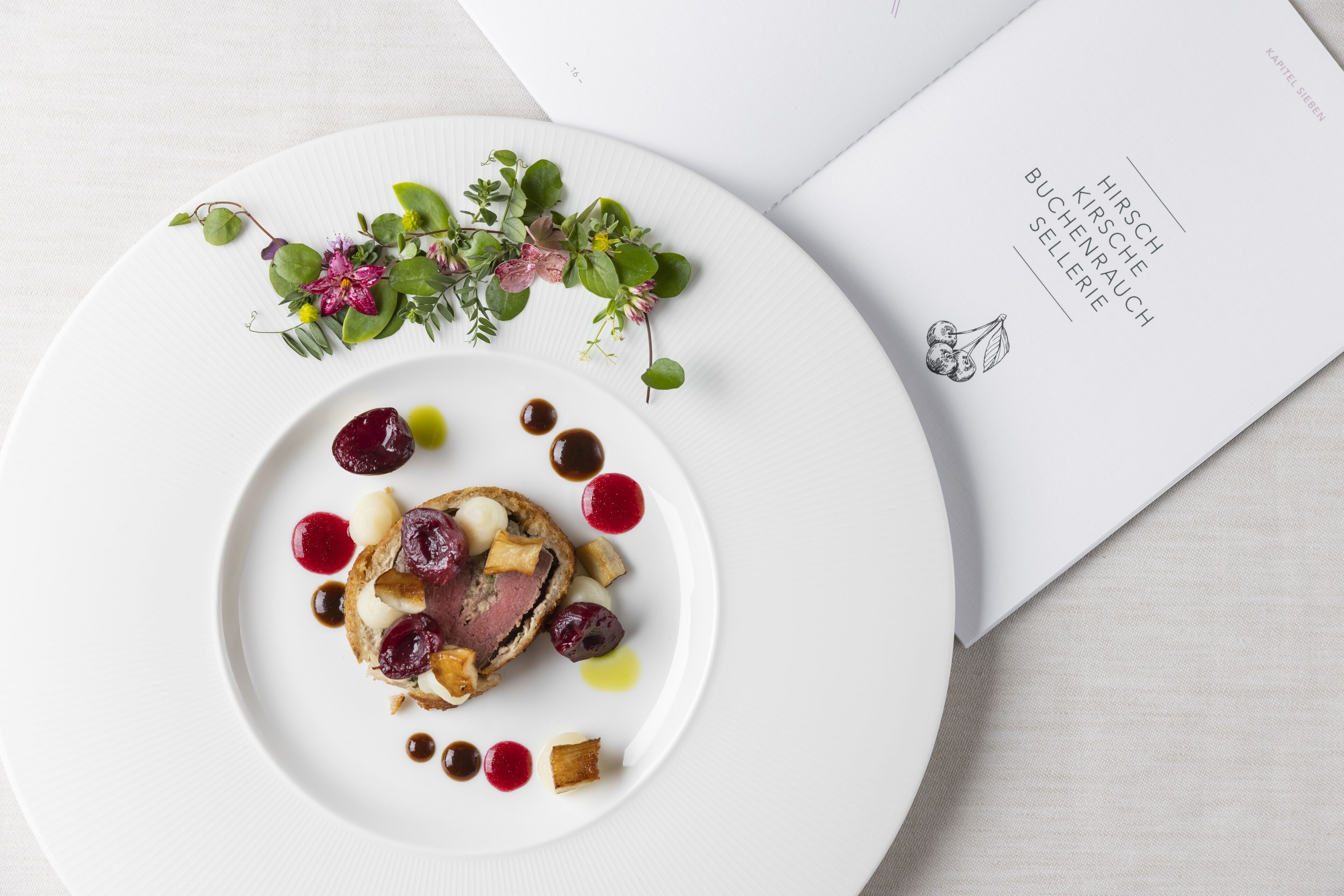 Une assiette blanche contenant un plat de viande, agrémenté de baies et de sauce, est posée sur une table où se trouve un menu.