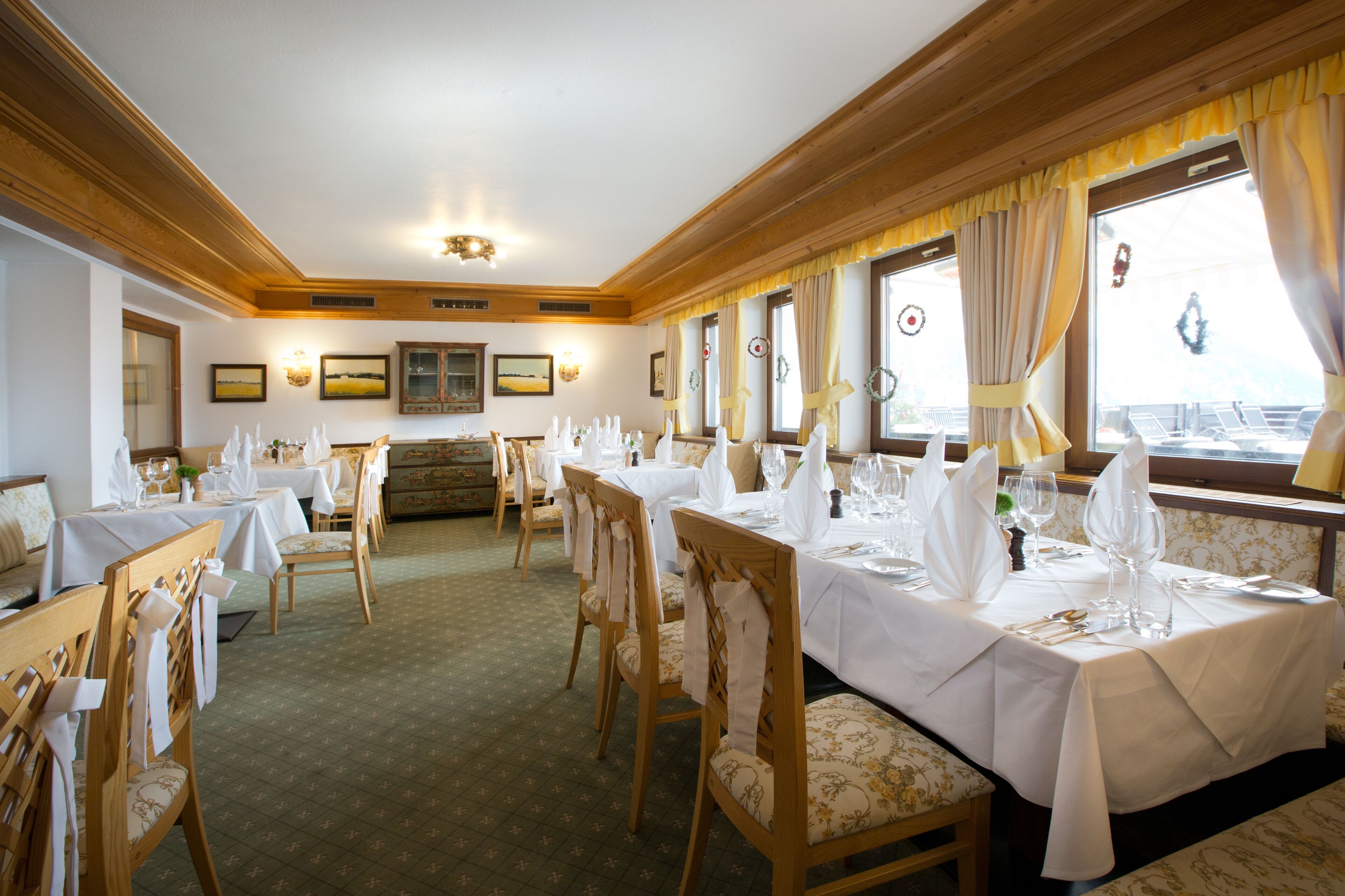 A dining area with tables set for service, wooden chairs, and a view of the outdoors through large windows.