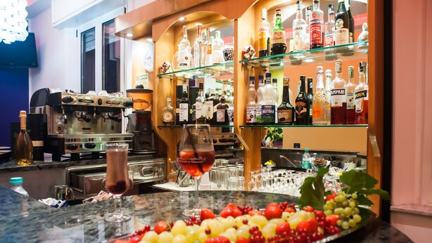 A bar area with a coffee machine, a variety of liquor bottles, and a fruit platter on the counter. - Hotel Angelini (Rimini)