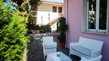 Un área de patio con mobiliario de mimbre blanco, una mesa de vidrio y plantas en macetas.