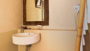 A bathroom with a white sink, a wooden-framed mirror, a wicker stool, and a bamboo towel rack.