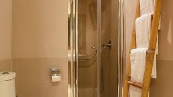 A bathroom with a glass-enclosed shower, a toilet, and a wooden towel rack.