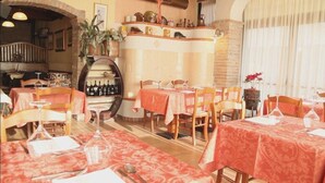 A restaurant with multiple tables, each covered with a red tablecloth. There are chairs around the tables, and a wine rack is visible in the background. - Locanda Canareggio (San Biagio di Callalta)