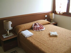 A neatly made bed with a brown bedspread, two bedside lamps, a folded white towel, and a small bag on the bed. - Locanda Canareggio (San Biagio di Callalta)