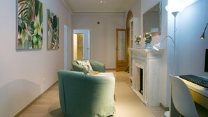 A living room with a green armchair, a white fireplace, and a desk with a computer. - Blanc Guesthouse (Barcelona)
