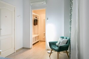 A hallway with a green armchair, a white door, and a closet with hanging clothes. - Blanc Guesthouse (Barcelona)