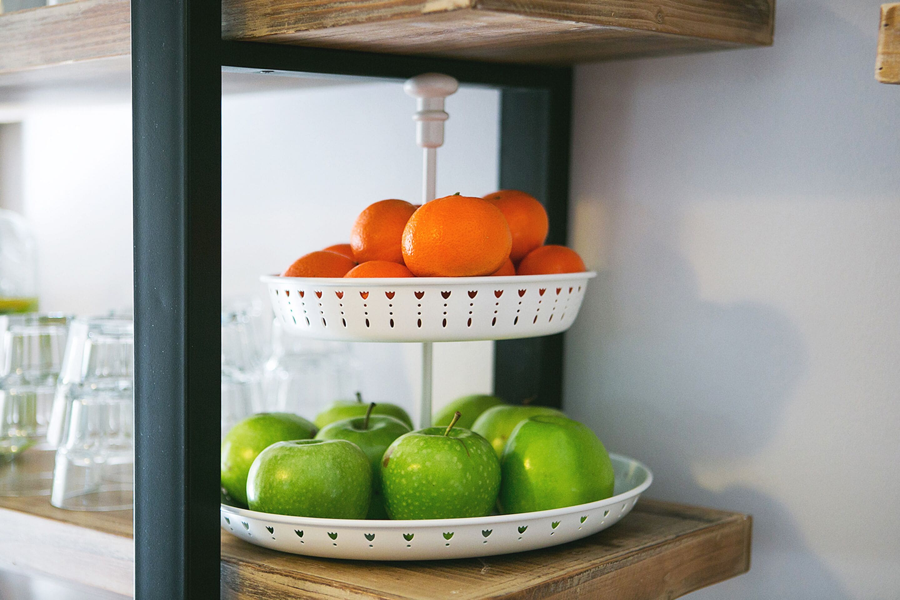 Un puesto de frutas de dos niveles con naranjas y manzanas verdes.