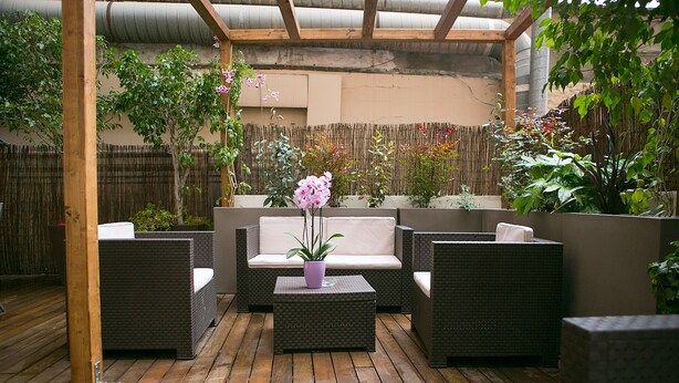 An outdoor patio with wicker furniture, a cushioned bench, and potted plants. - Blanc Guesthouse (Barcelona)