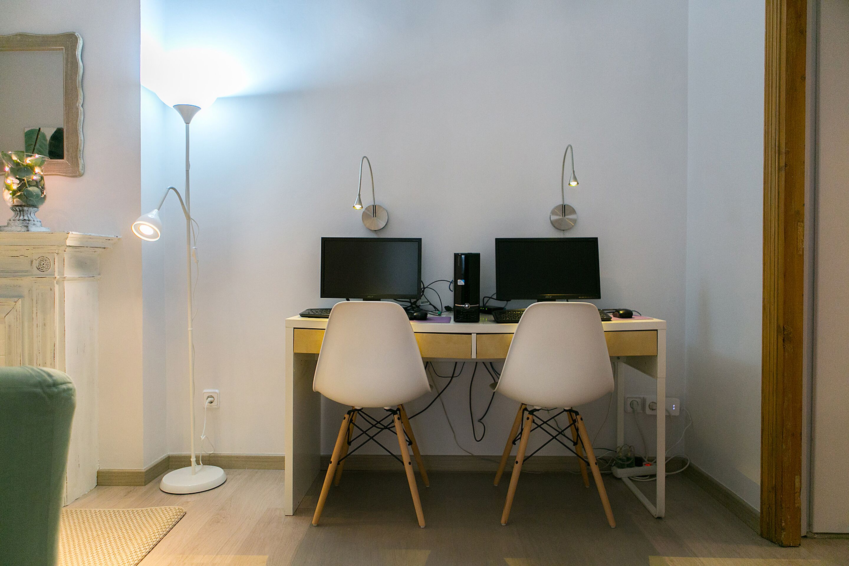 A room with a desk, two chairs, two monitors, a lamp, and a small plant.