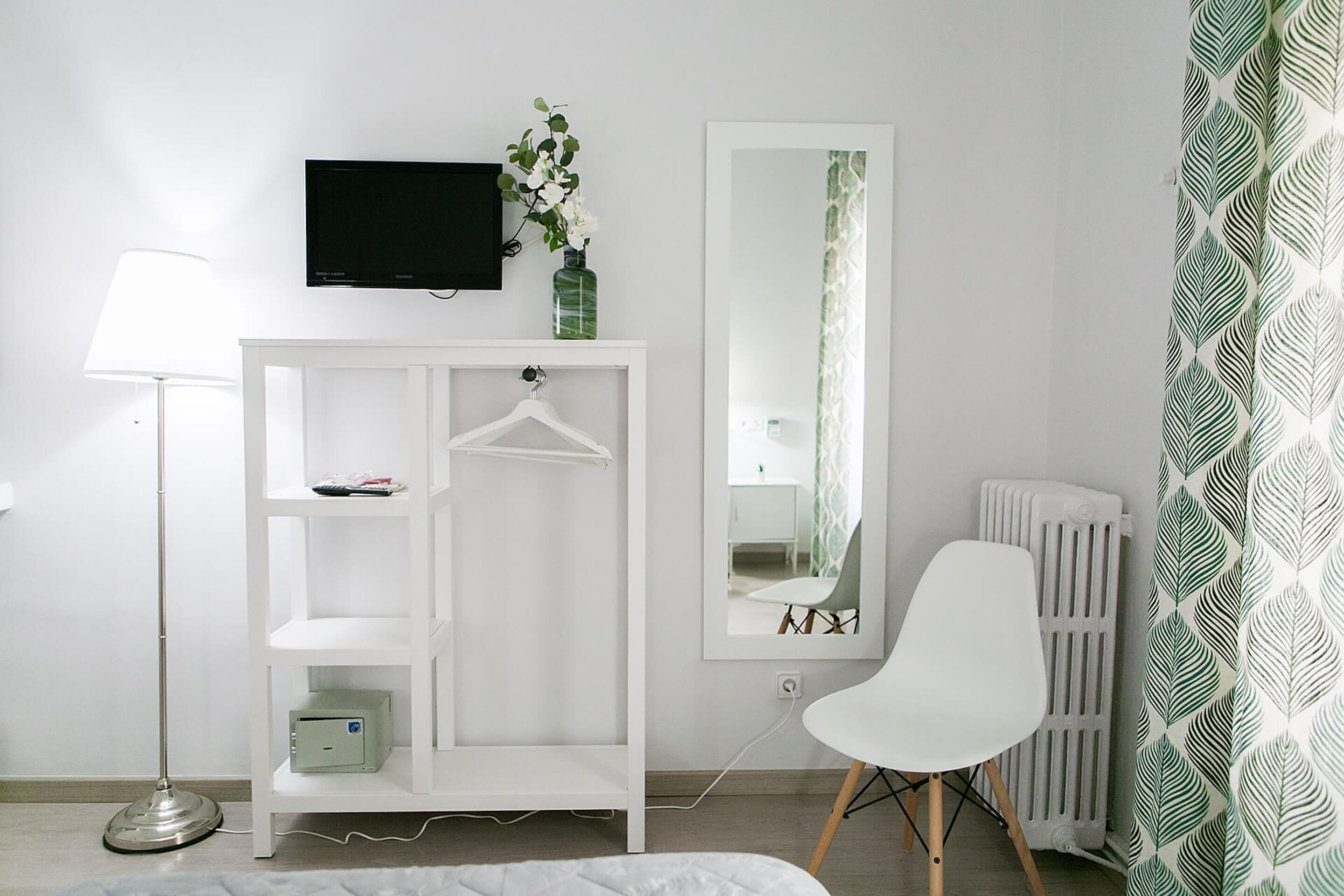 A modern room with a white wardrobe, a flat-screen TV, a white chair, and a radiator.