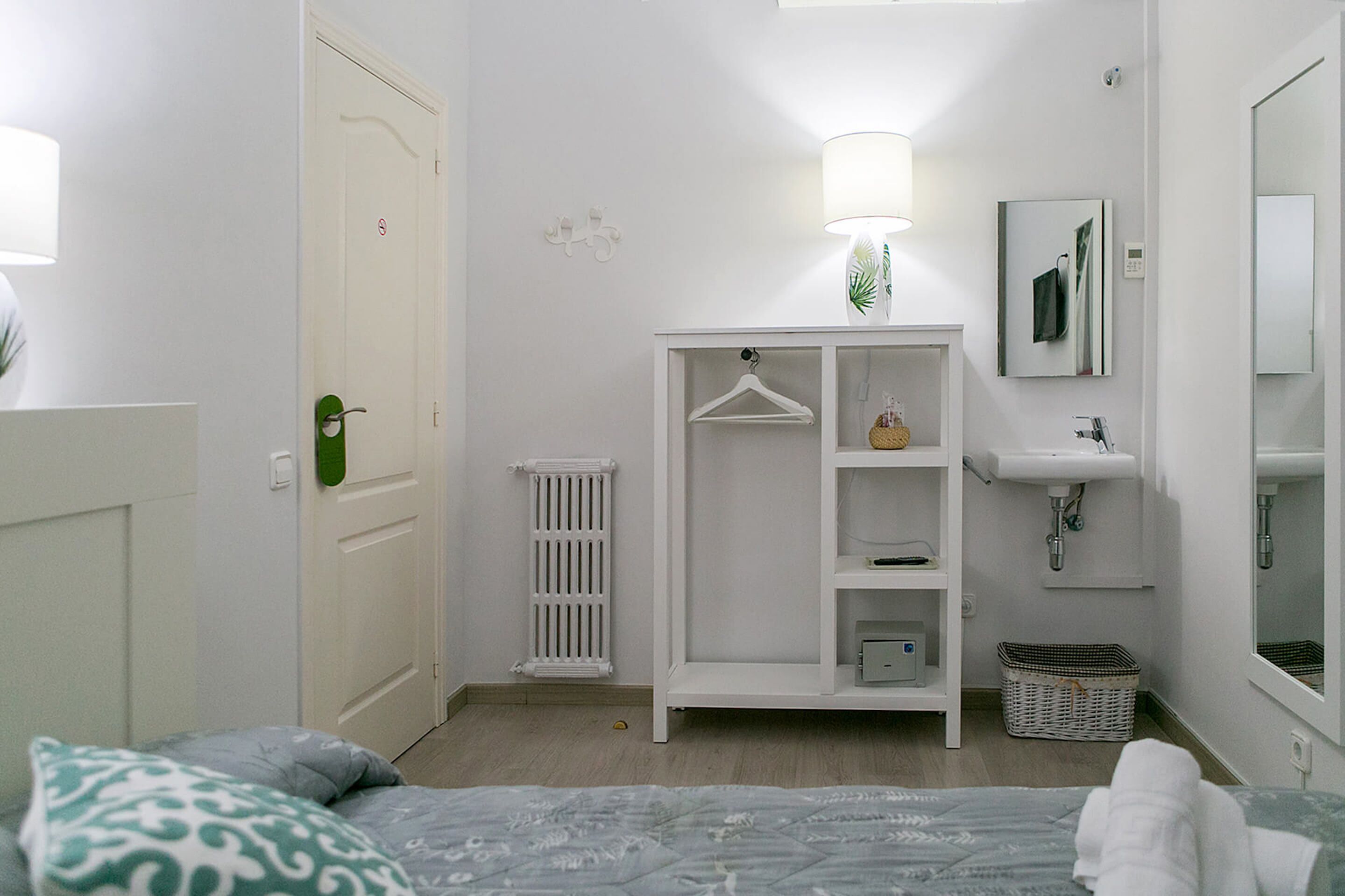 A bedroom with a bed, a wardrobe, a radiator, a hanging lamp, a mirror, and a sink.