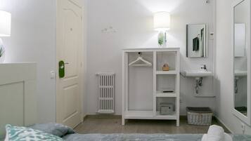 A bedroom with a bed, a wardrobe, a radiator, a hanging lamp, a mirror, and a sink.