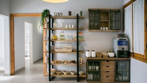 A kitchen with wooden shelves stocked with various food items, a coffee machine, and a cabinet with glass doors. - Blanc Guesthouse (Barcelona)