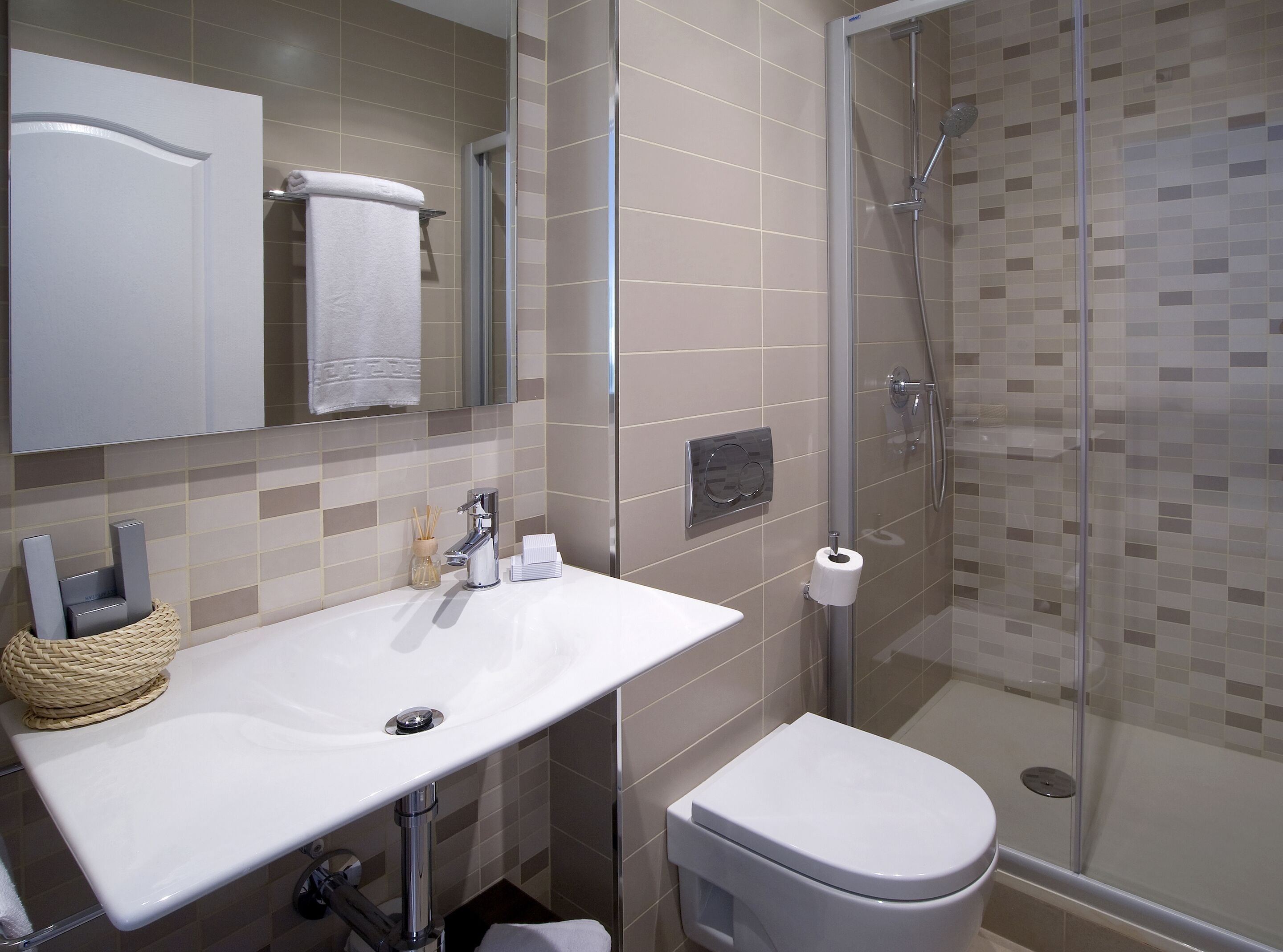 Un baño moderno con un lavamanos blanco, un inodoro y una ducha con cerramiento de vidrio.