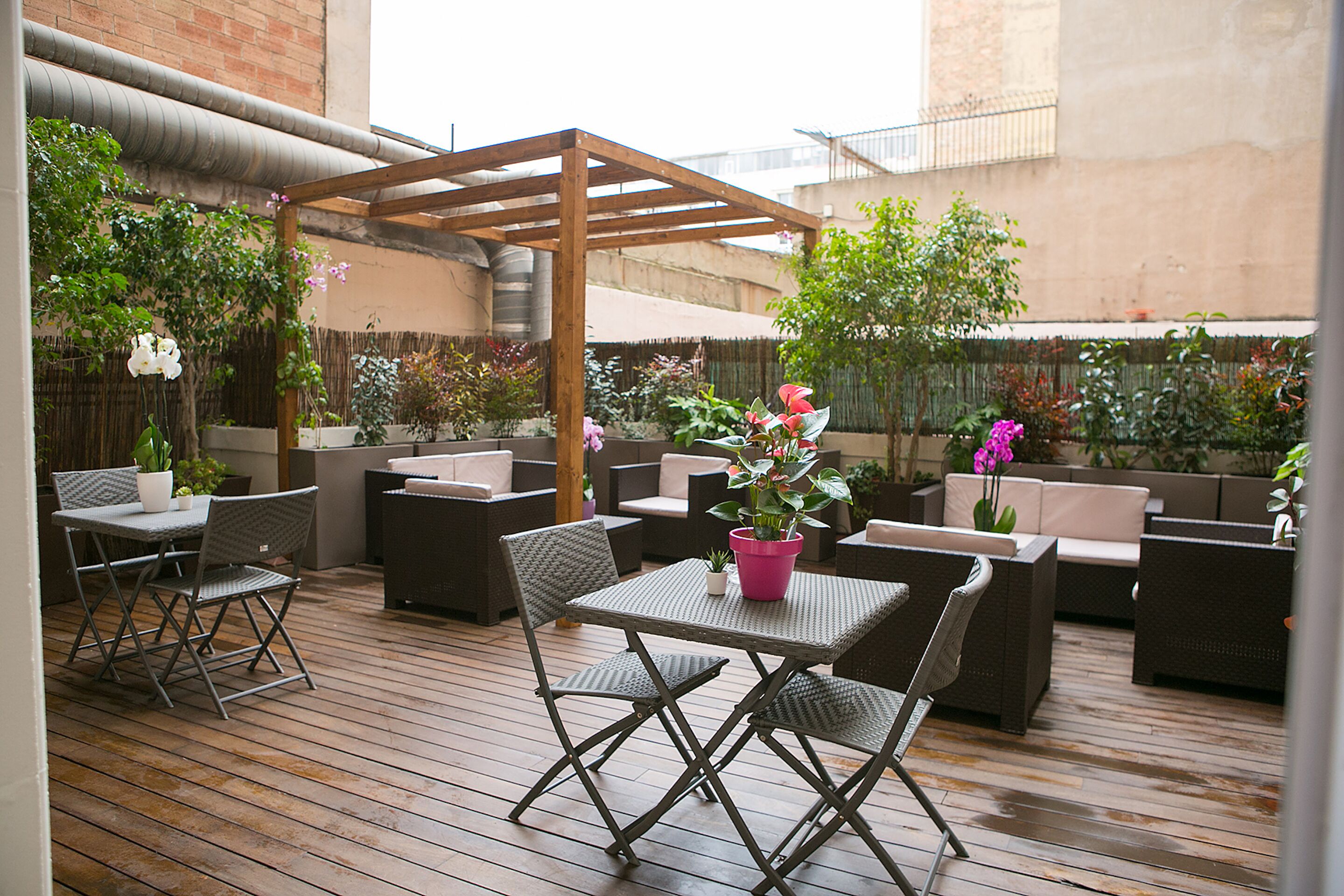 Un patio al aire libre con piso de madera, mobiliario de mimbre y plantas en macetas.