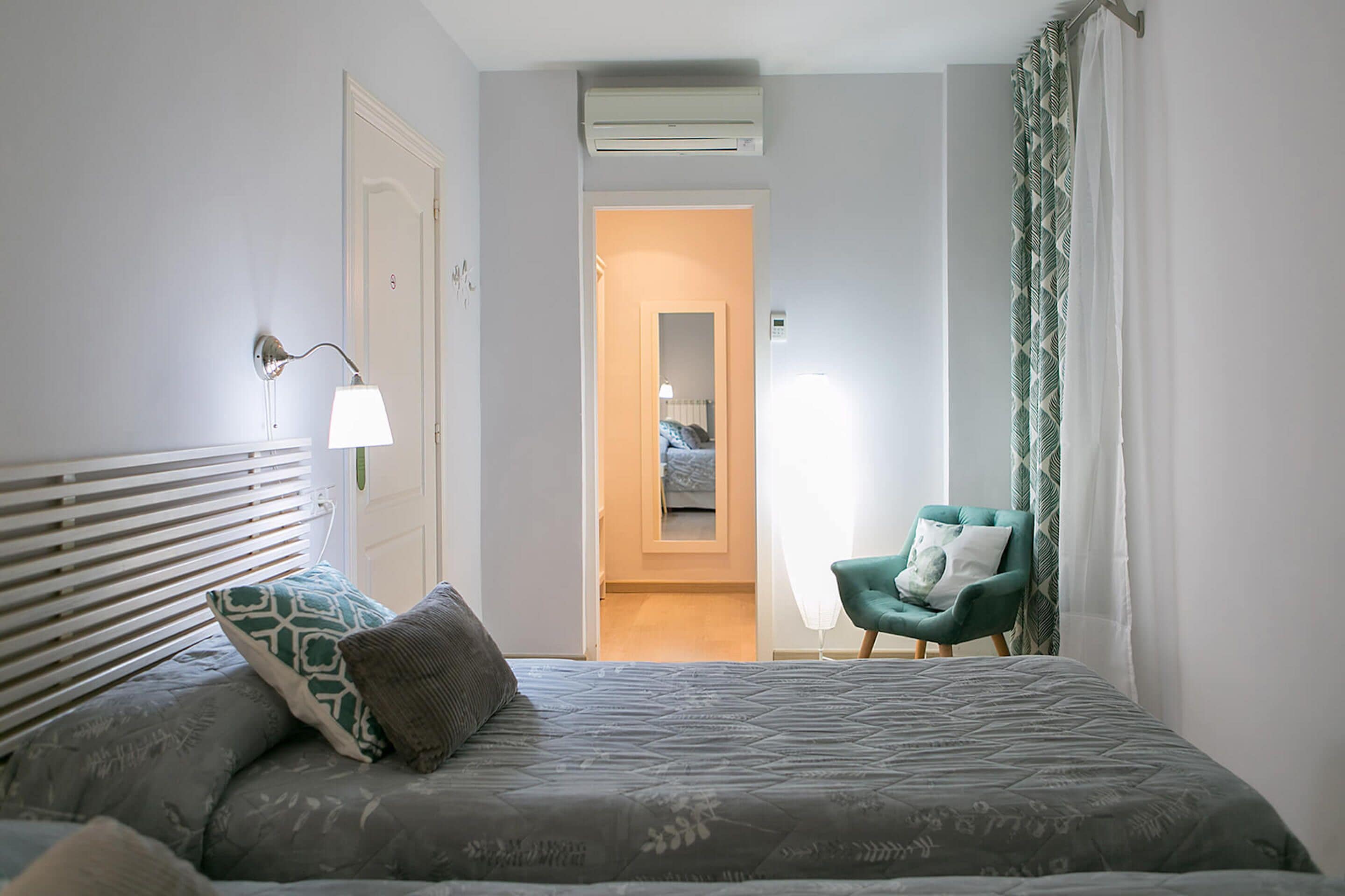 Un dormitorio con cama, una silla, una lámpara y un pasillo que conduce a otra habitación.