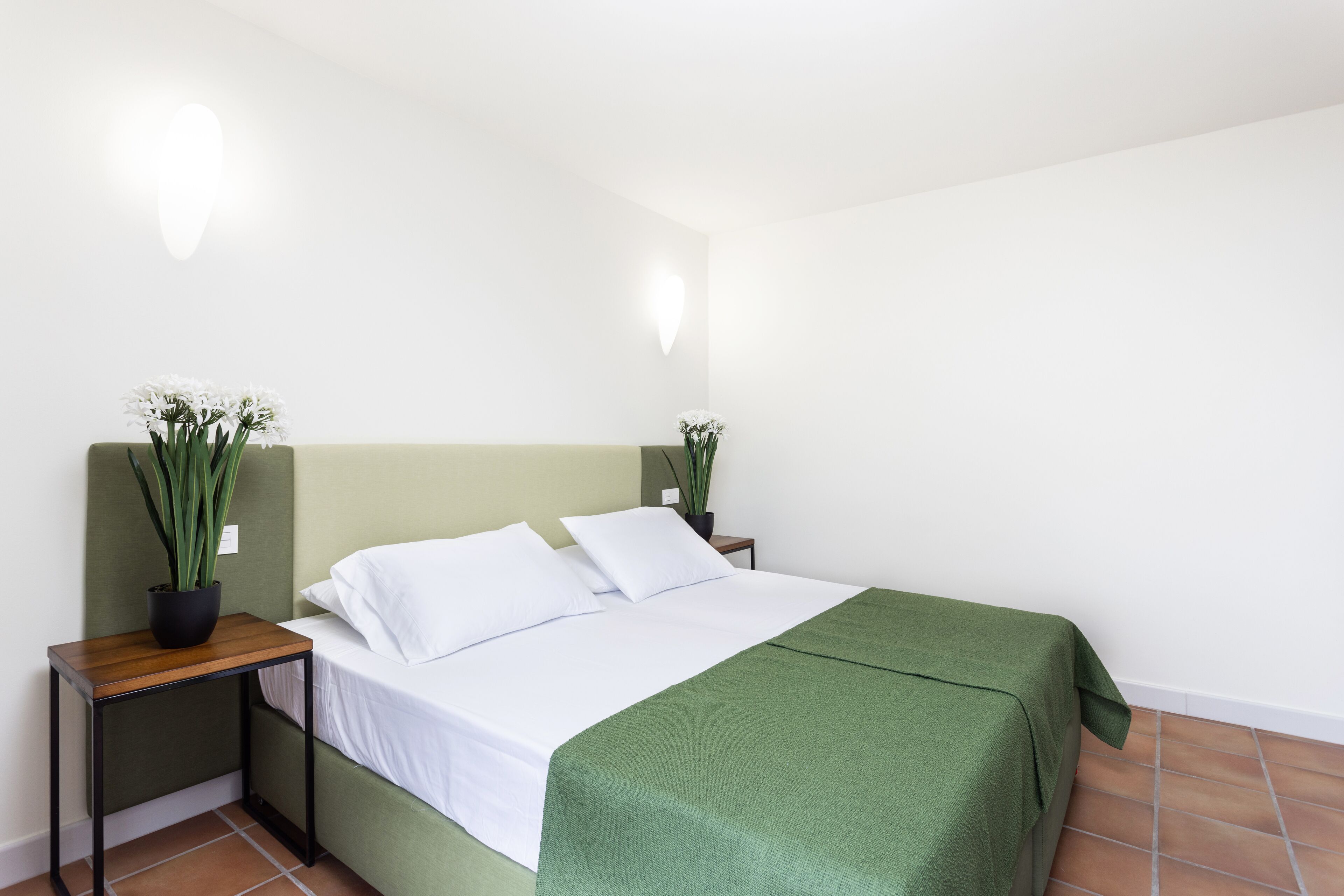 Una habitación de hotel ordenada con una cama, una mesita de noche y una planta en maceta.