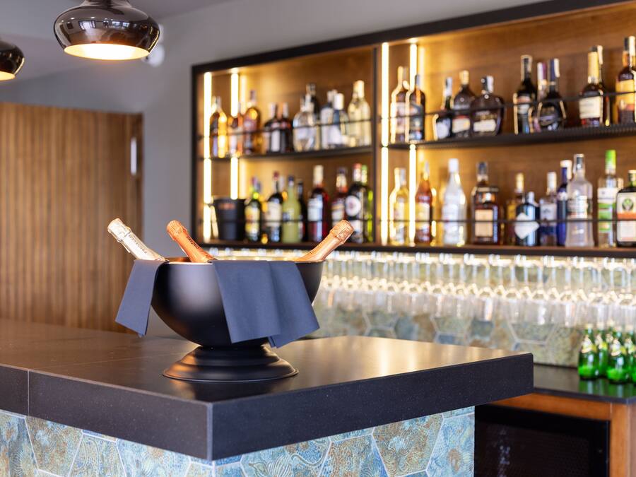 Eine Bar mit einer schwarzen Arbeitsplatte, einer Schüssel mit Brotstangen und Regalen voller Spirituosenflaschen.