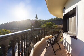 A balcony with a view of a hilly landscape, a chair, and a window with a light fixture. - Hotel Alta Montaña (Vilaflor)