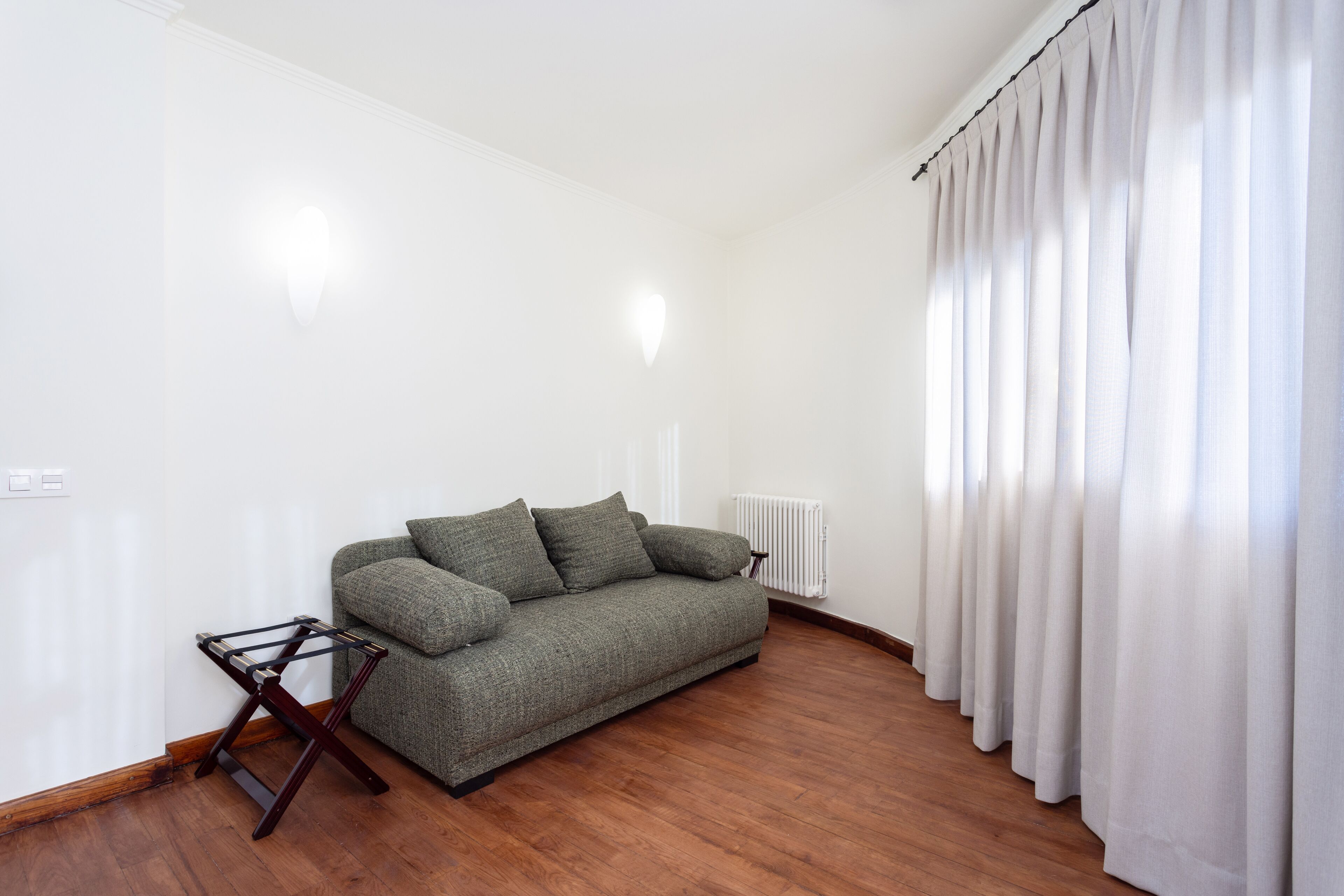 A modern living room with a green sofa, a wooden coffee table, and white curtains.