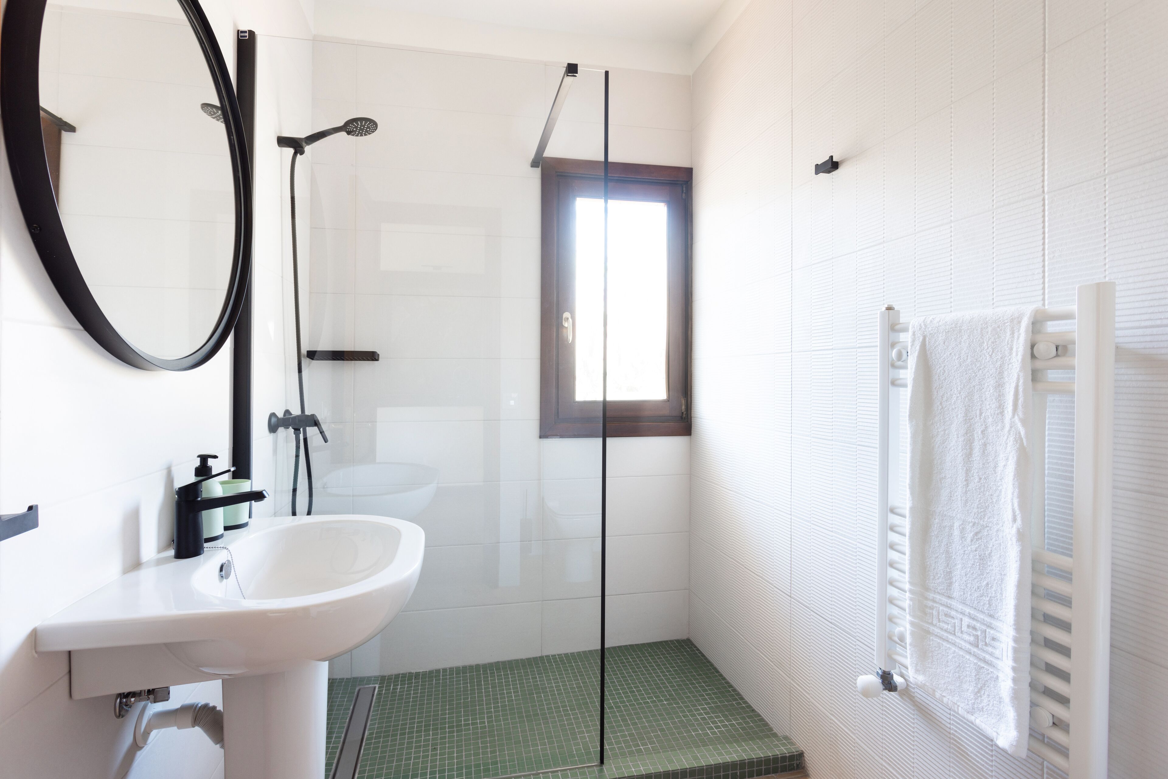 A modern bathroom with a glass shower enclosure, a white sink, and a towel rack.