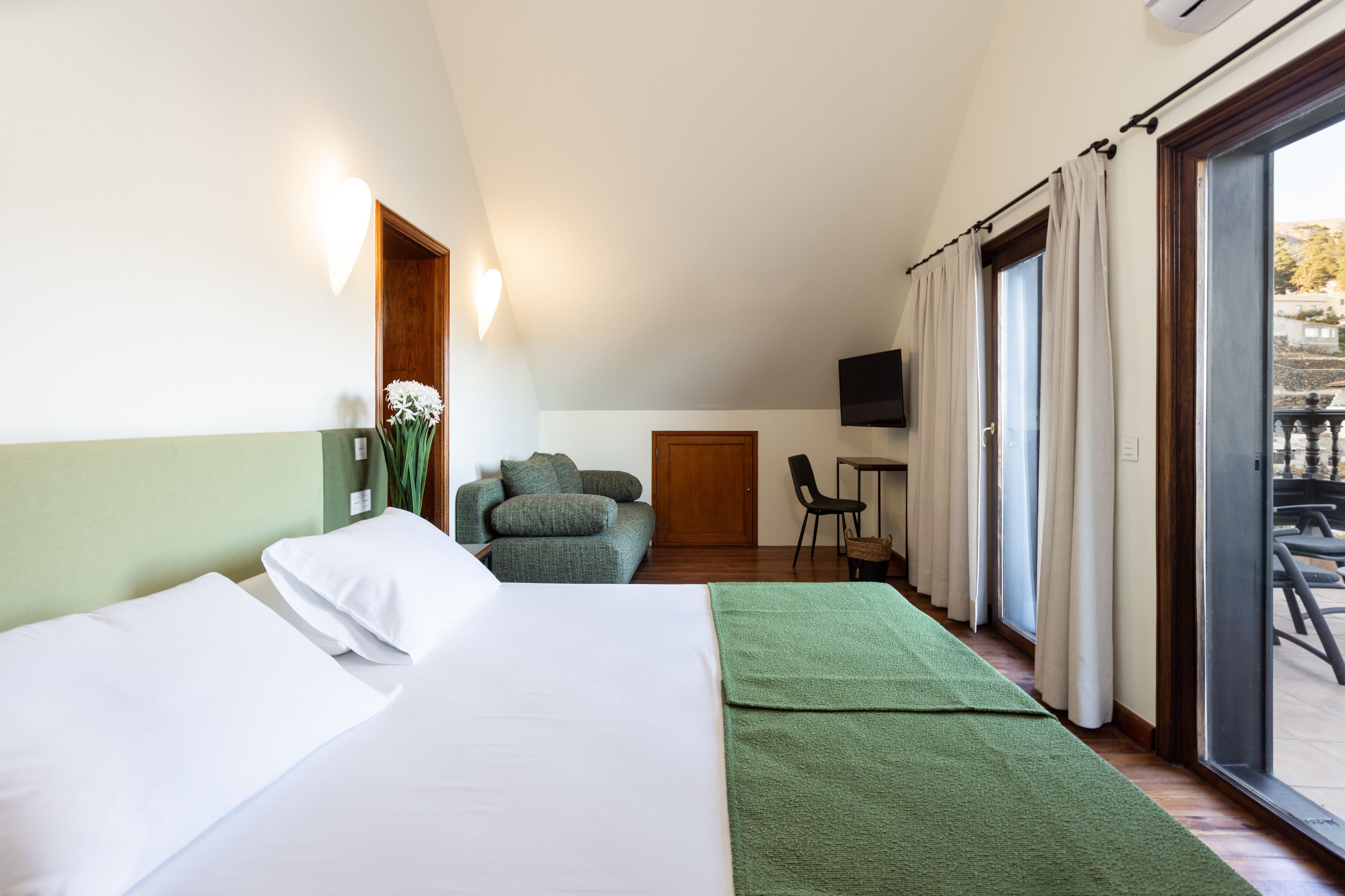 A hotel room with a bed, a green sofa, a small table, and a TV.