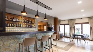 A bar area with a tiled backsplash, bar stools, and a variety of bottles. There is a dining area with a table and chairs. - Hotel Alta Montaña (Vilaflor)