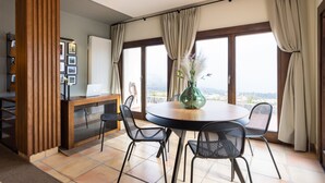A modern dining area with a round table, four chairs, a laptop on a wooden desk, and a vase with flowers. - Hotel Alta Montaña (Vilaflor)