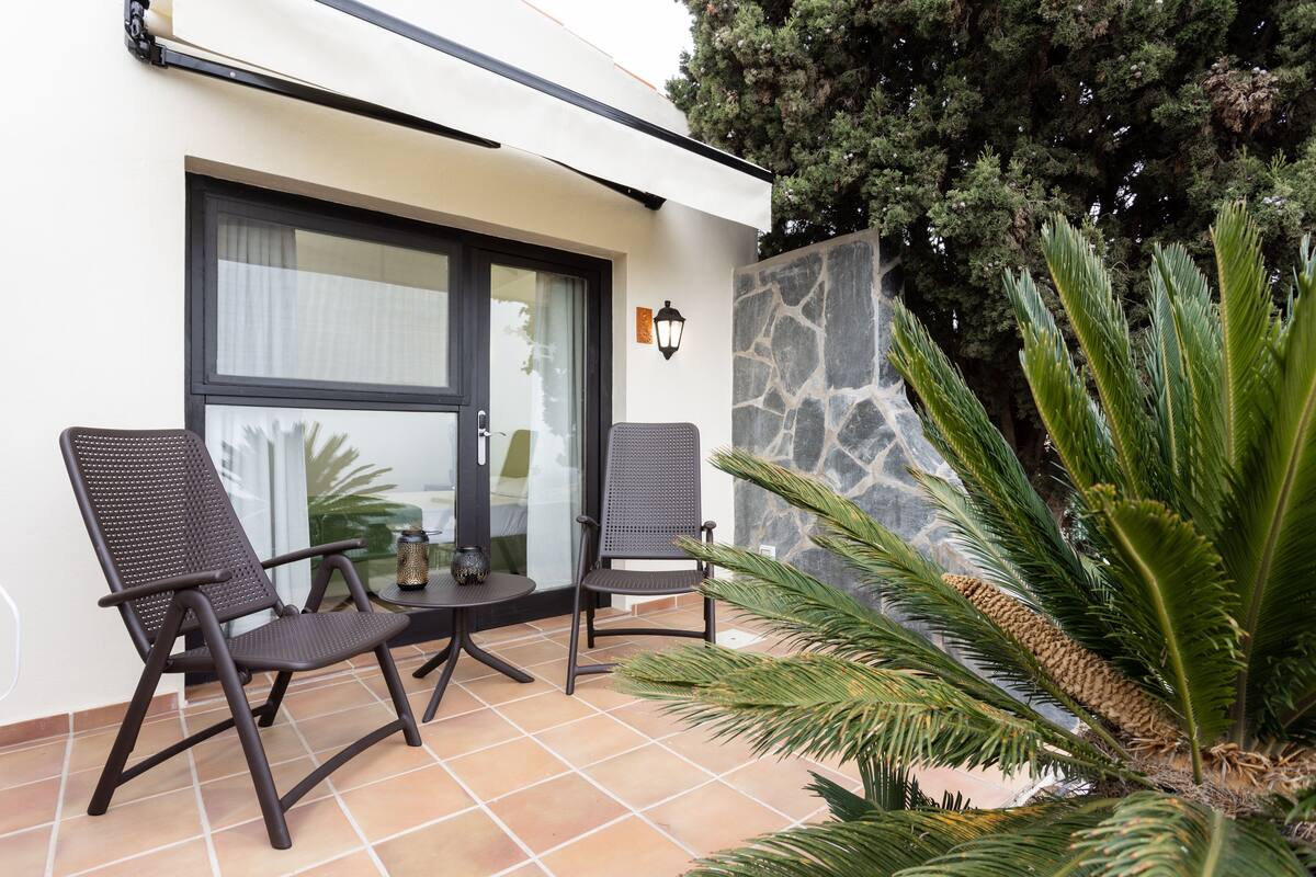 An outdoor seating area with two chairs and a table, a stone wall, and a large plant.