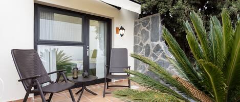 An outdoor seating area with two chairs and a table, a stone wall, and a large plant.
