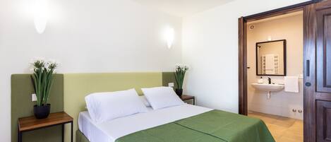 A neatly arranged bedroom with a bed, bedside tables, a green bedspread, and potted plants.