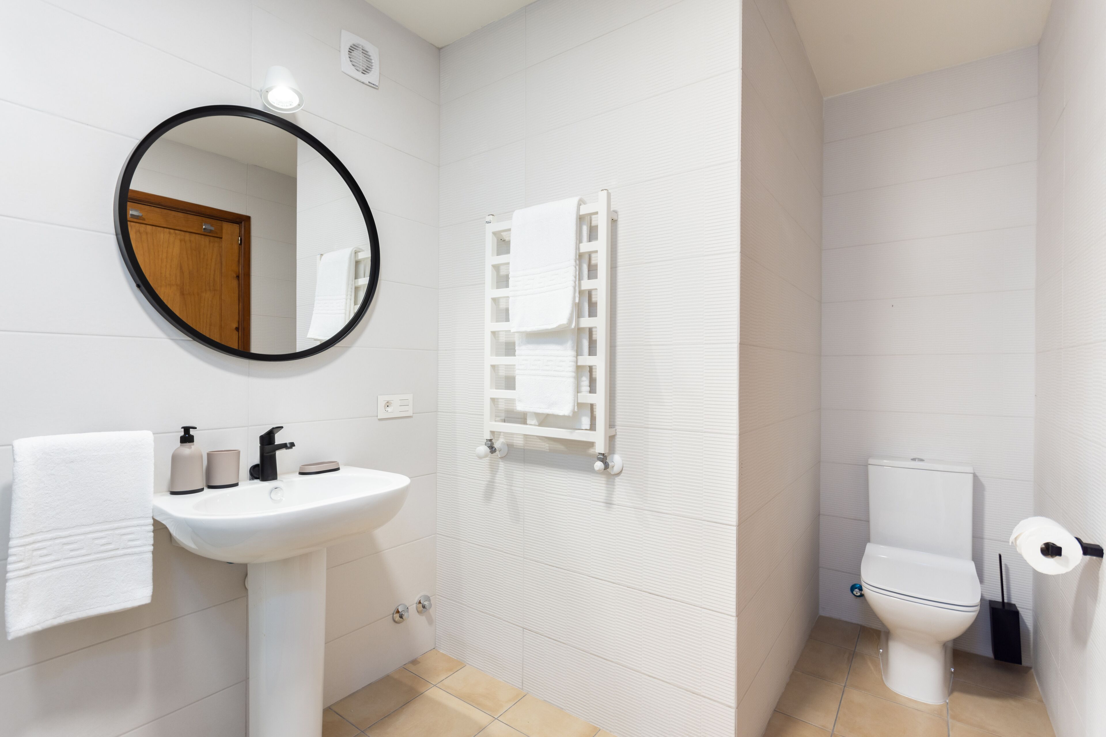 A bathroom with a white sink, mirror, towel rack, toilet, and a white towel on the wall.