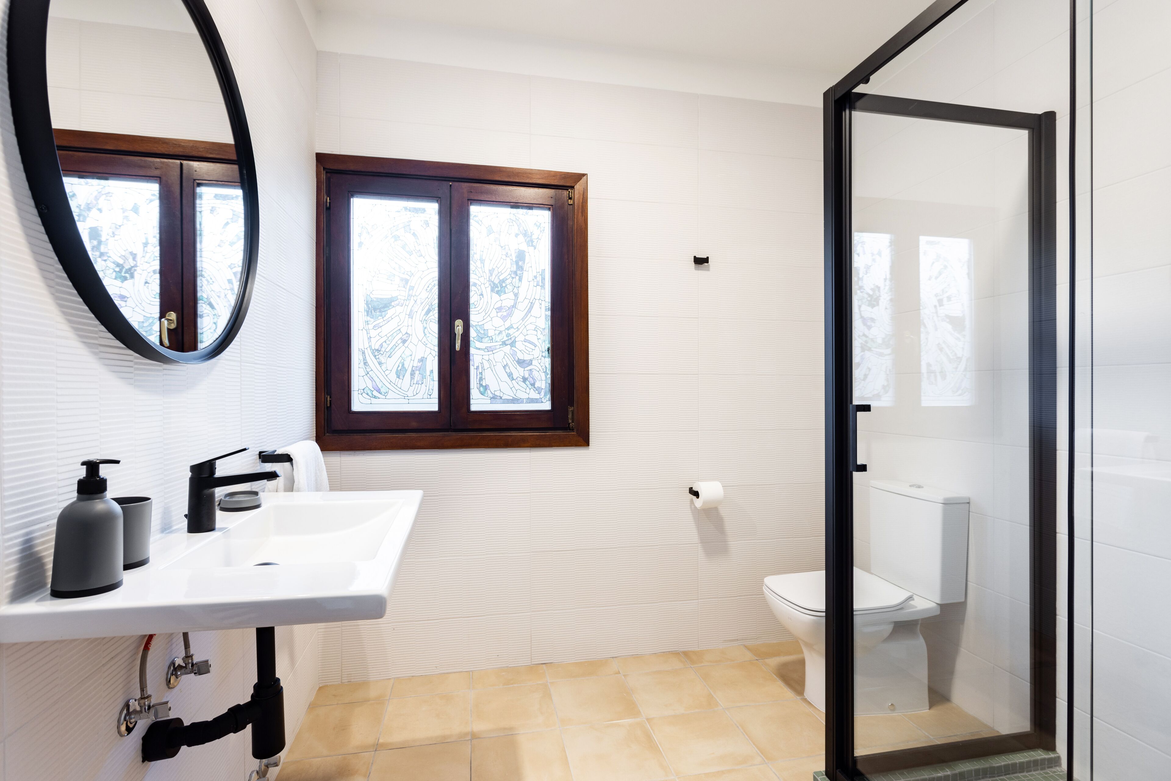 Un bagno con lavandino bianco, specchio, finestra e vaso da bagno.