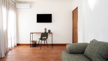 Una sala de estar con piso de madera, un sofá verde, un sillón negro, una mesita con objetos decorativos y un televisor montado en la pared.