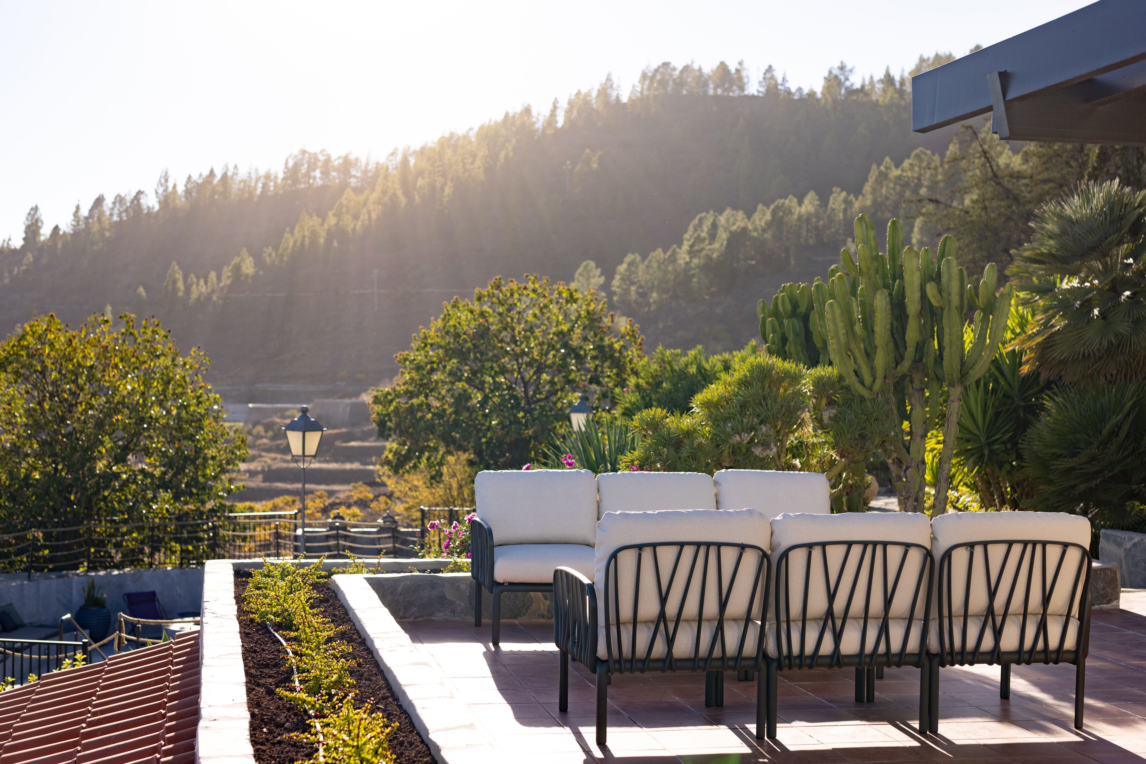 A patio with outdoor seating, a view of a forested hillside, and a stone pathway.