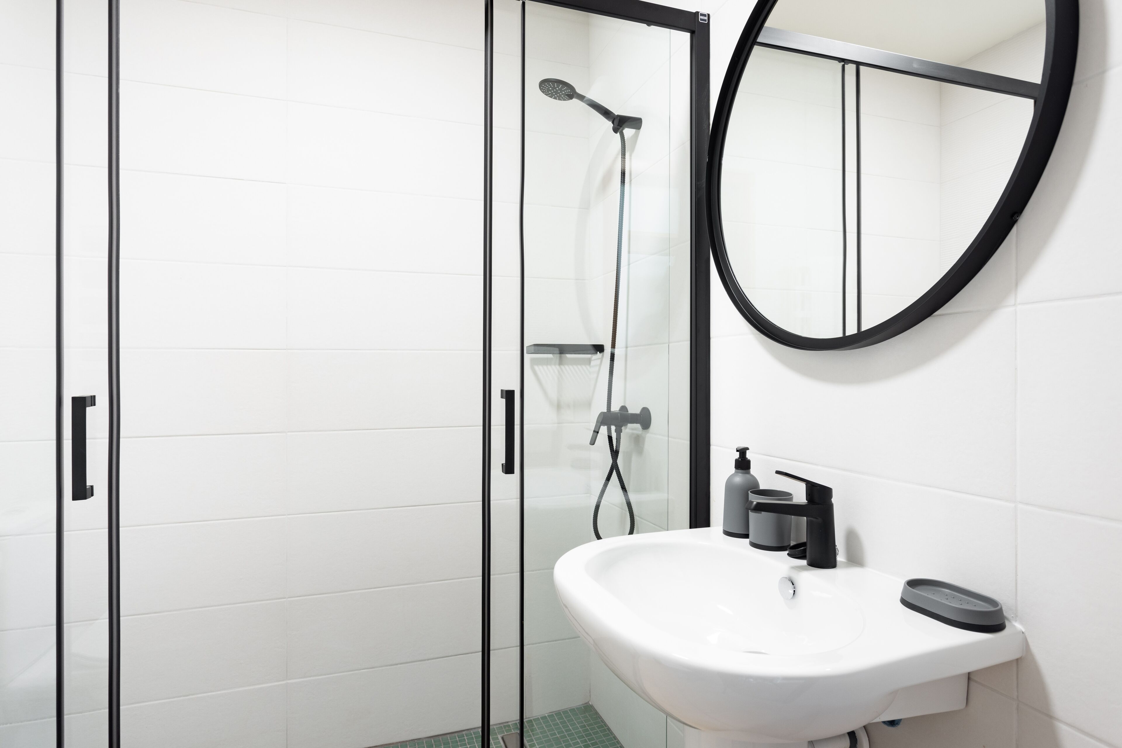 Une salle de bain moderne avec une douche à parois de verre, un lavabo blanc et un miroir rond.