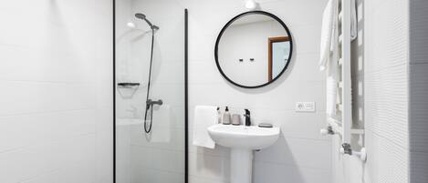 A modern bathroom with a glass-enclosed shower, a pedestal sink, and a round mirror.