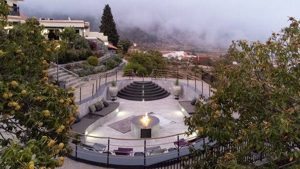 A circular outdoor seating area with a central fire feature, surrounded by stone steps and greenery. - Hotel Alta Montaña (Vilaflor)