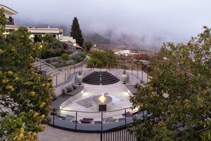 A circular outdoor seating area with a central fire feature, surrounded by stone steps and greenery. - Hotel Alta Montaña (Vilaflor)