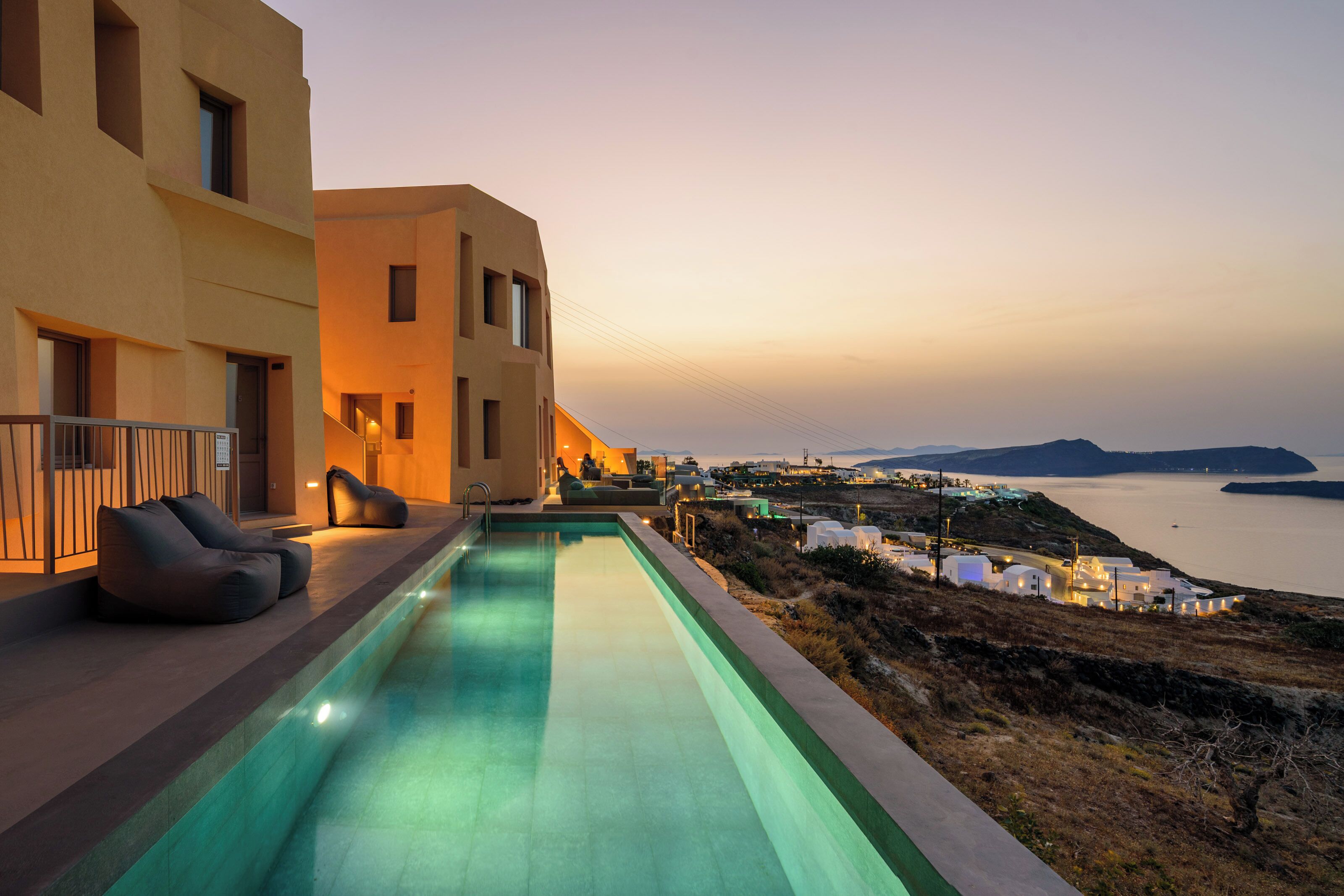 Zona junto a la piscina con vista al mar y a islas distantes, arquitectura moderna y mobiliario exterior.