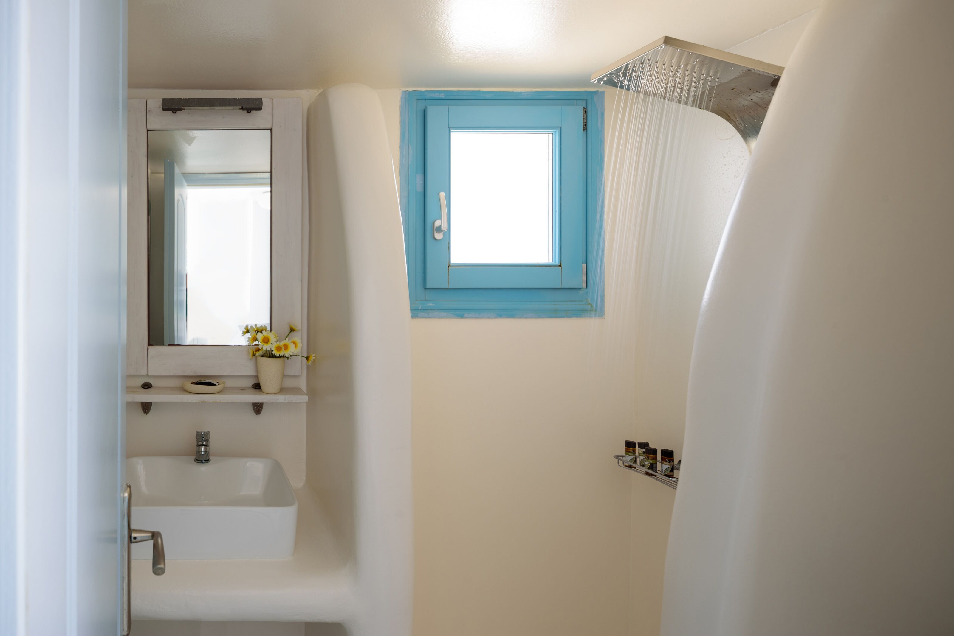 Un baño con lavamanos blanco, un espejo, una puerta azul y una cortina de ducha.