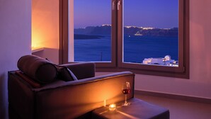 Una habitación moderna con un amplio ventanal corredera que da a un balcón con vistas al mar y luces de la ciudad a lo lejos.