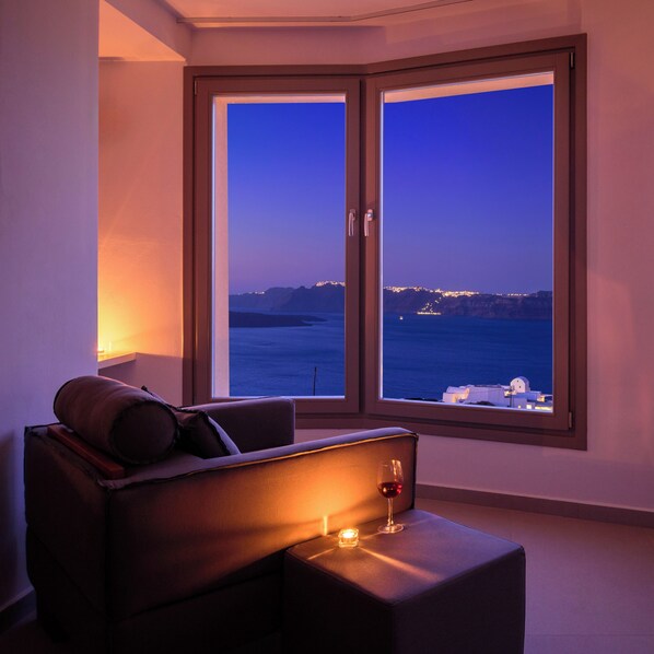 A modern room with a large sliding glass door leading to a balcony with a view of the sea and distant city lights. - Kalestesia Suites (Santorini)