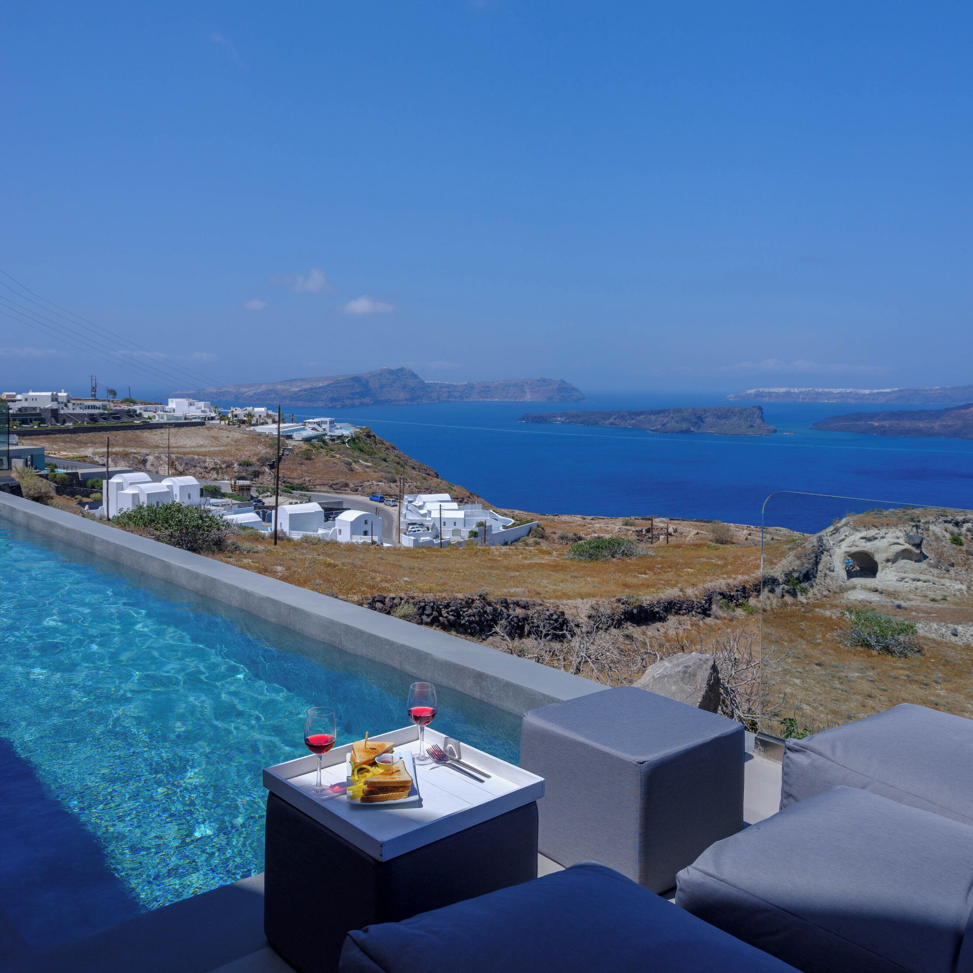 Ein Poolbereich mit Blick auf eine Küstenlandschaft, darunter weiße Gebäude und ein klares, blaues Meer.