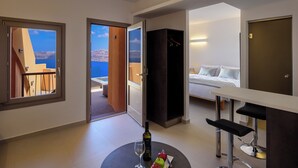 Habitación de hotel con balcón, cama, zona de comedor y minibar.