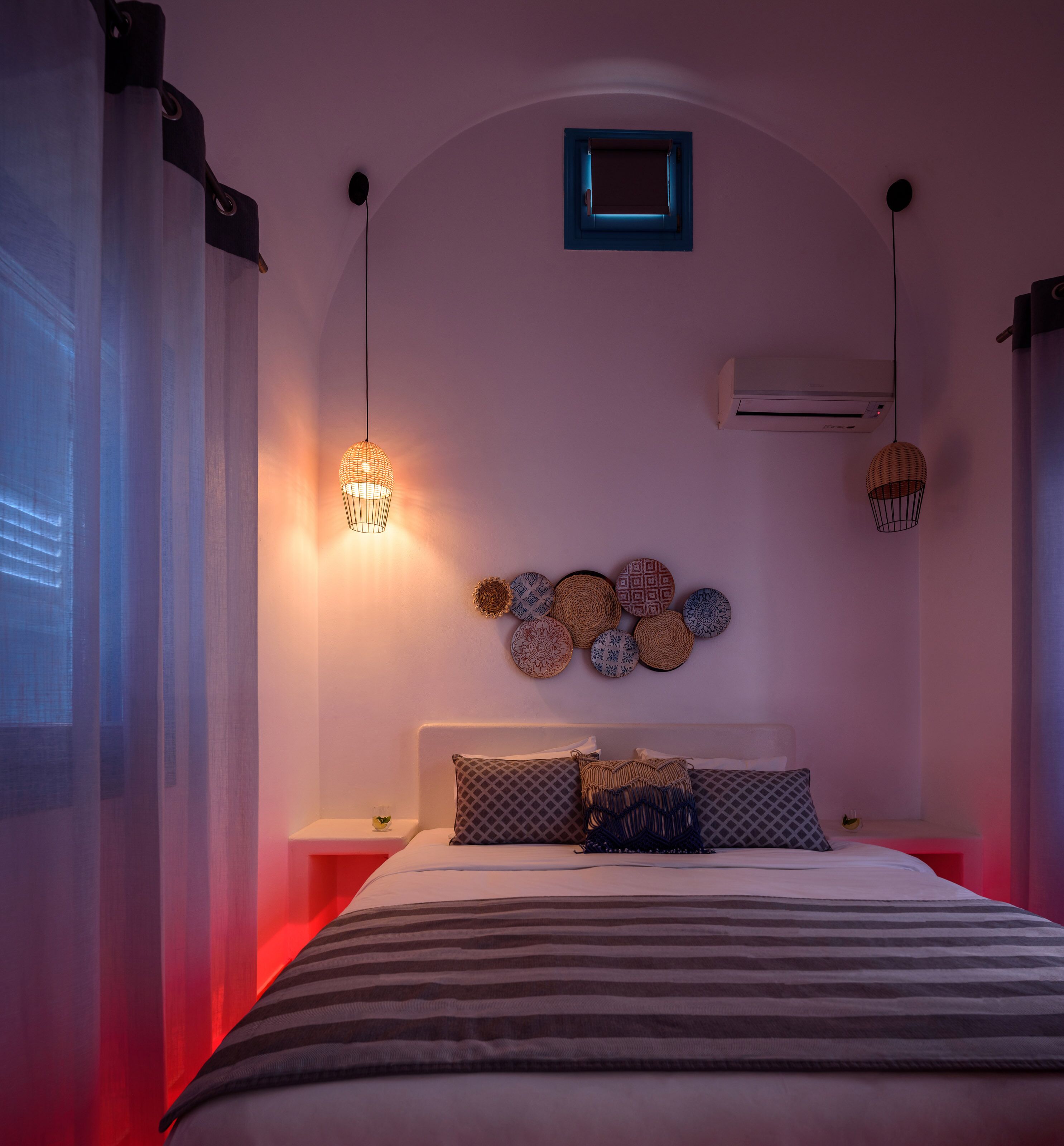 A bedroom with a bed, bedside tables, a wall-mounted air conditioner, and decorative wall plates.