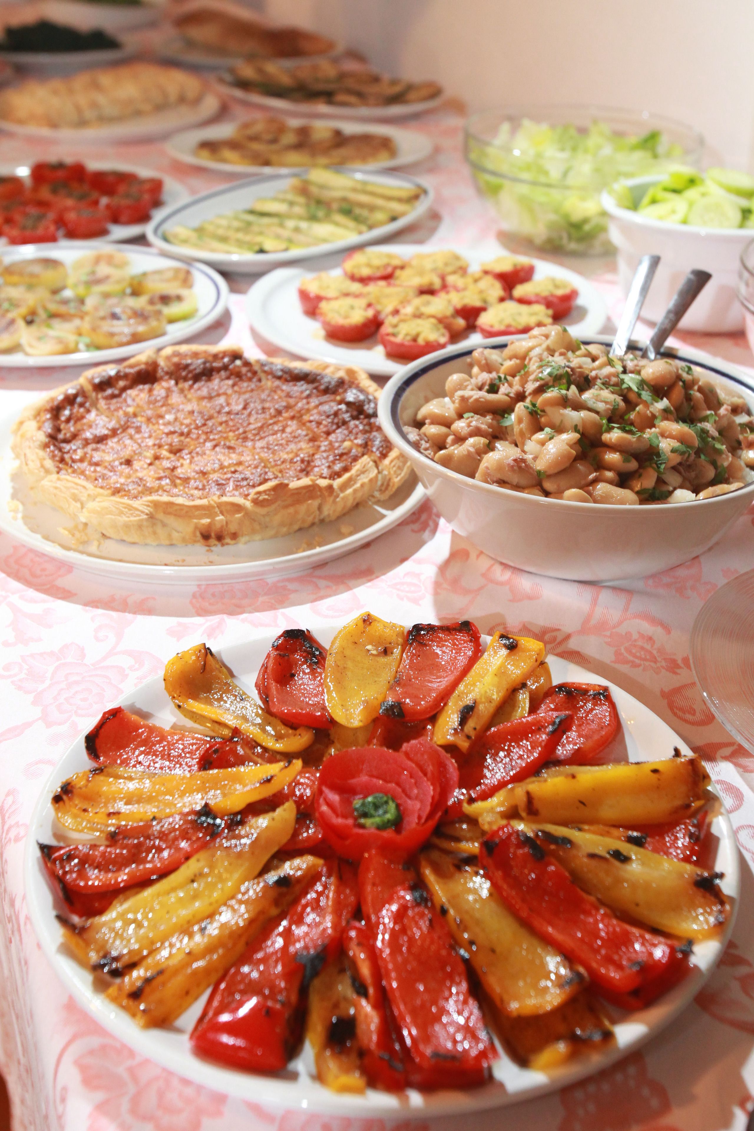 Une table où l’on trouve divers plats, notamment une quiche, une salade de haricots et des légumes rôtis.