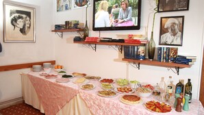 A room with a dining table set with various dishes, a television mounted on the wall, and shelves with books and decorative items. - Hotel San Vitale (Medicina)